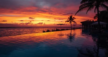 Infinity Pool eines Erwachsenenhotels bei Sonnenuntergang mit Palmen und Meerblick